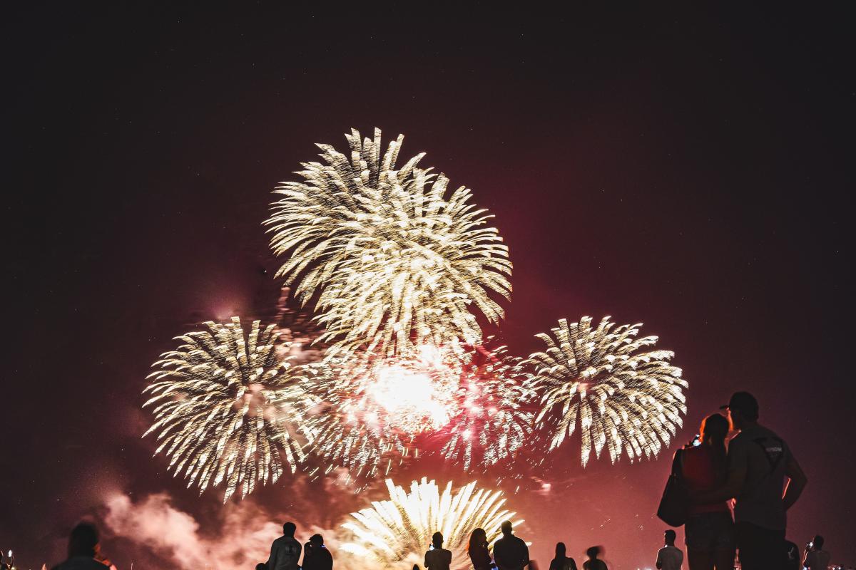 A crowd of silhouetted beachgoers watch a night-time fireworks display during Territory Day