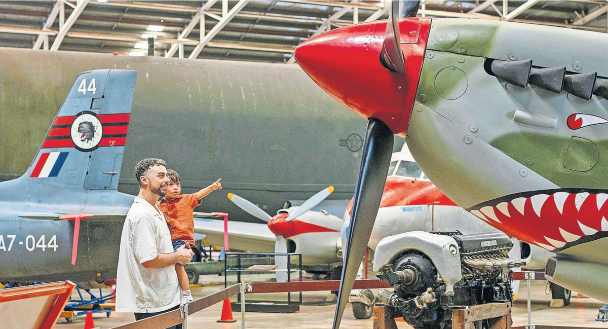 Father Holds his young son as they look up to a World War 2 era fighter jet at the Darwin military museum